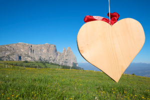 the shape of a wooden heart, in the background the Scilir, Alpe di Siusi (Seiser Alm), Castelrotto (Kastelruth), Dolomites, South Tyrol, Italy the shape of a wooden heart, in the background the Scilir, Alpe di Siusi (Seiser Alm), Castelrotto (Kastelruth), Dolomites, South Tyrol, Italy